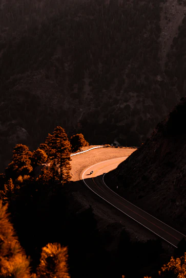 A motorbike riding towards the viewer on a twisting road bathed in warm evening sunlight, surrounded by the rugged Andalusian mountains.