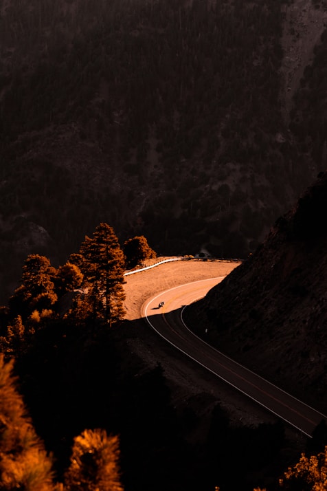 A moody, dark-toned image of a female biker on a winding mountain road.