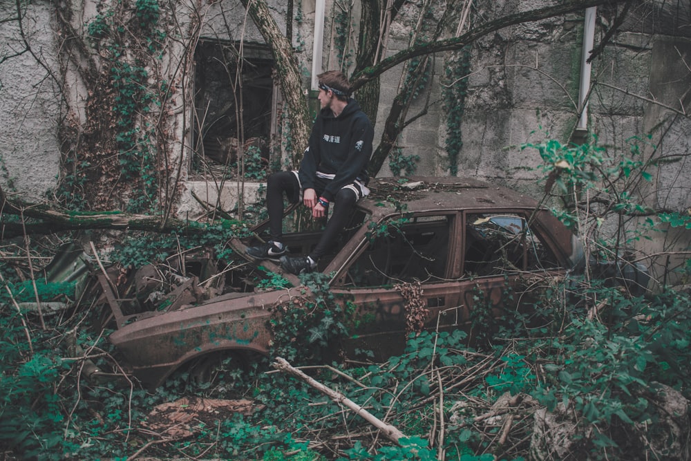 Mann sitzt auf dem Dach eines Fahrzeugwracks auf Fokusfotografie