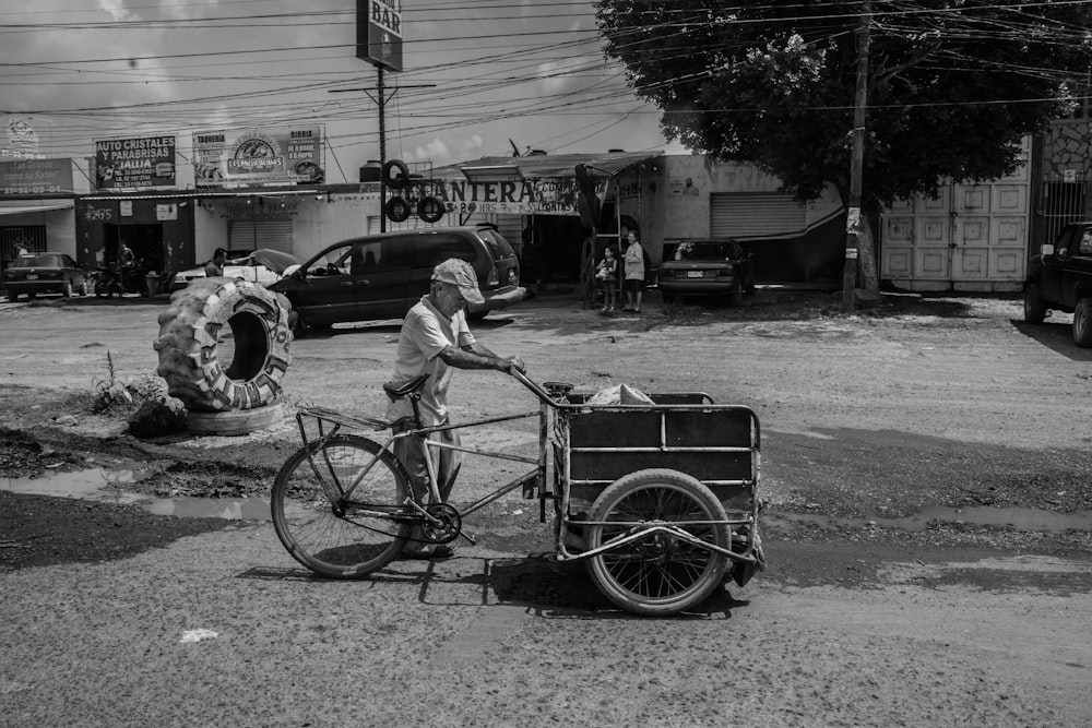 grayscale photography of man holding bicycle