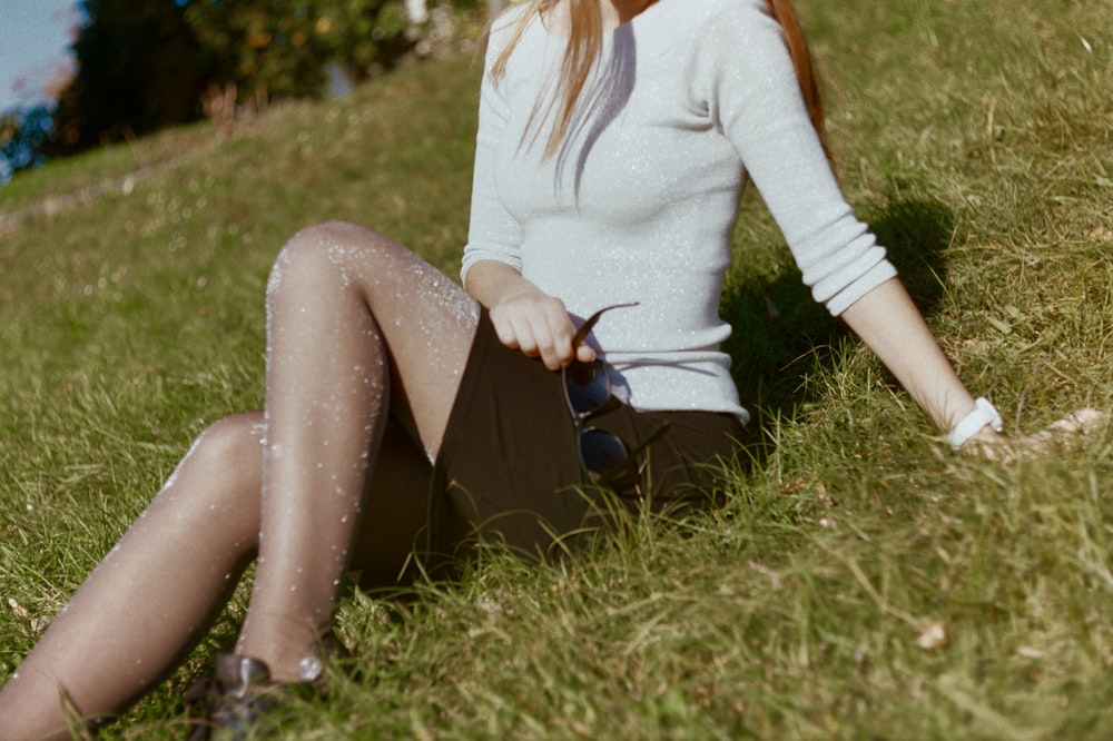 woman wearing white top and brown shorts sitting on grass field during daytime