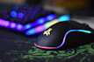 A close-up of a sleek gaming mouse glowing with customizable LED lights on a dark desk.