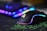A sleek gaming mouse with RGB lighting effects sits on a green and black mousepad. In the background, a blurred view of a keyboard with vibrant RGB lighting can be seen, adding a futuristic and colorful ambiance.