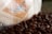 A close-up view of a coffee bag partially visible, surrounded by a scattered pile of roasted coffee beans. The bag has a geometric design with the words 'Boldly Go' and an established date of 2012 printed on it. The colors are warm, with a focus on browns and beiges.