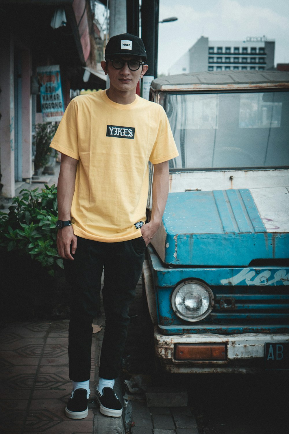 man in yellow tee shirt stand beside blue car parked on road side