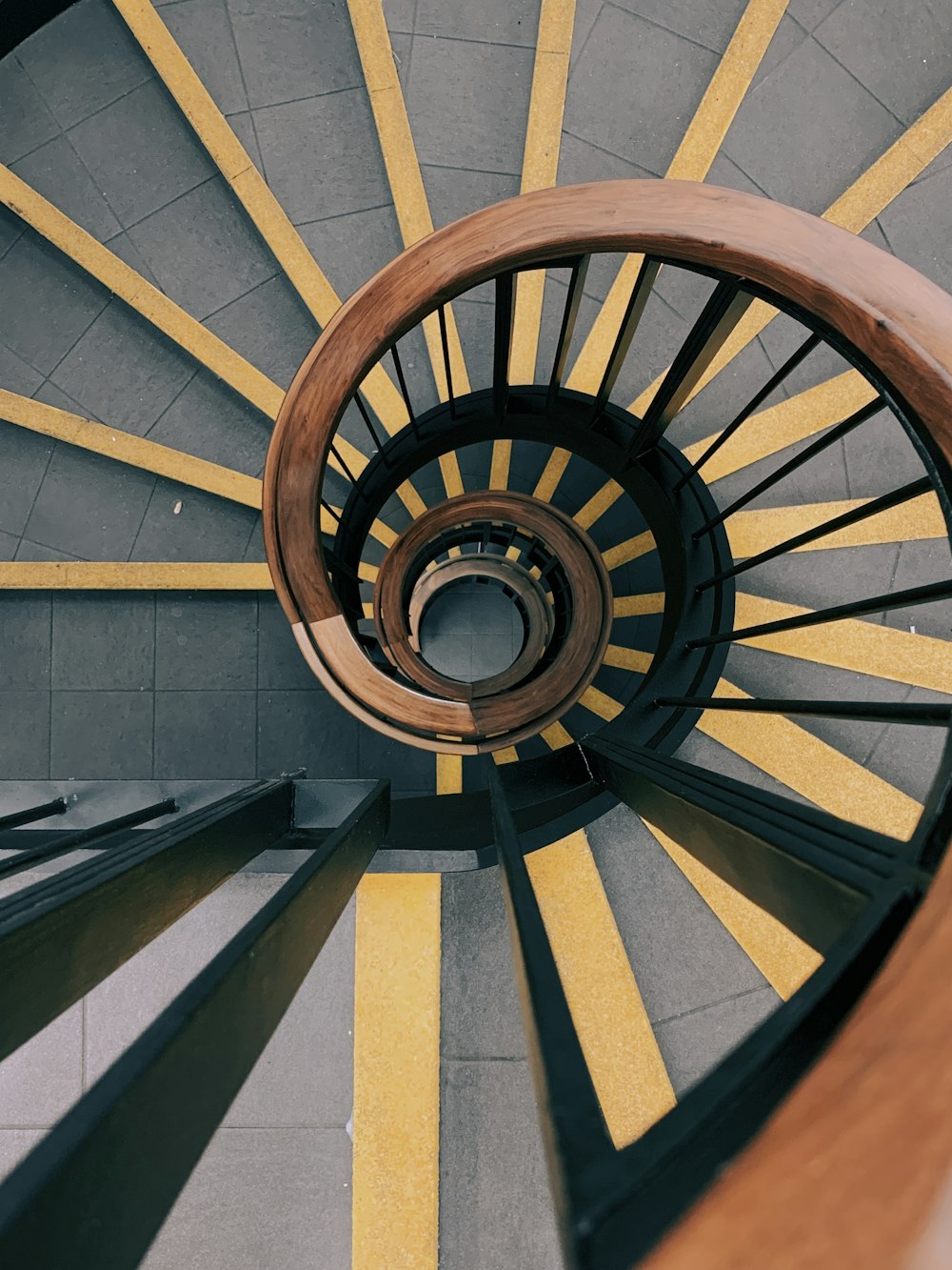 spiral gray and yellow concrete stair with brown rail