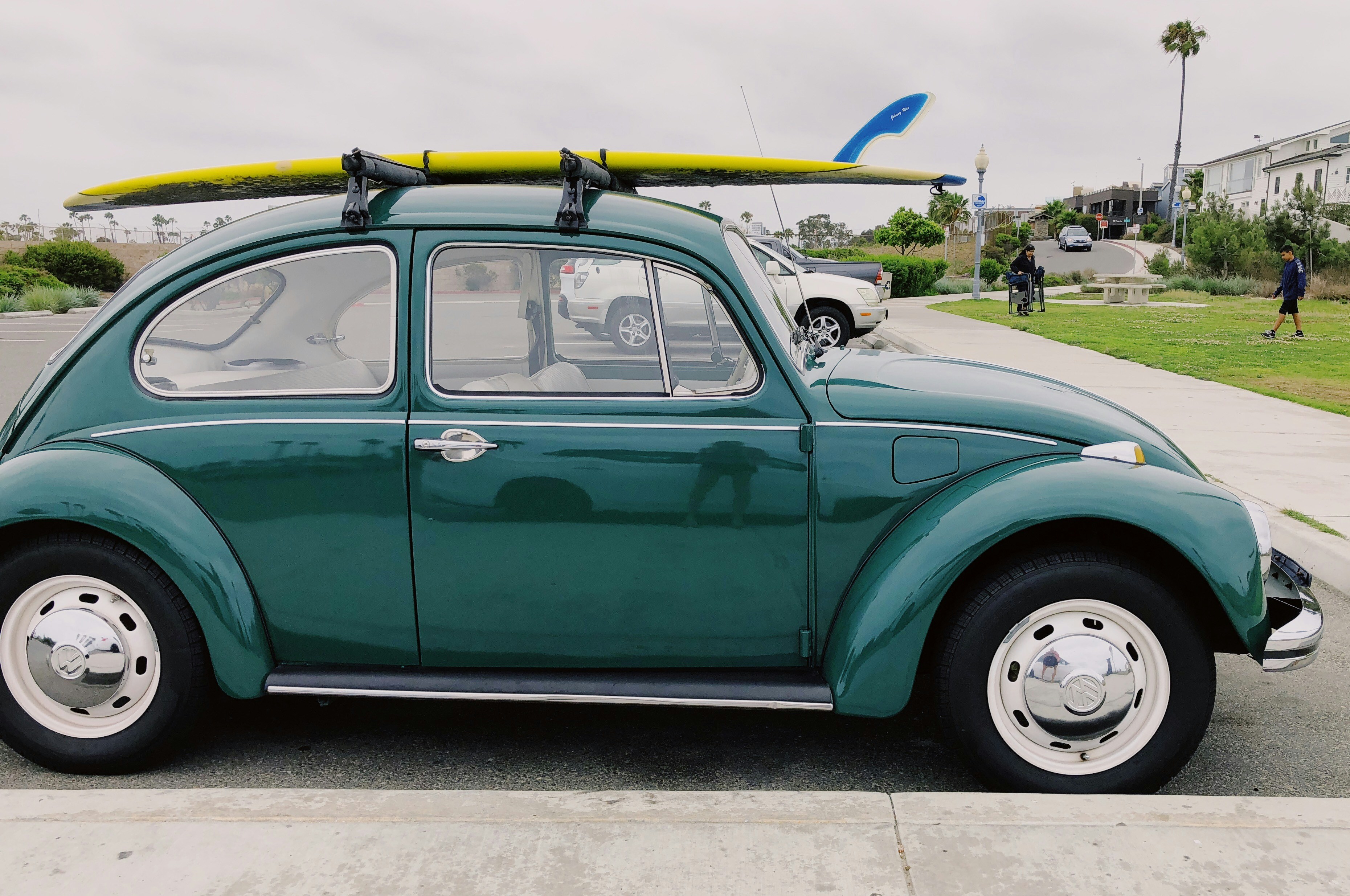 empty green Volkswagen Beetle carrying yellow surfboard on parking lot during daytime