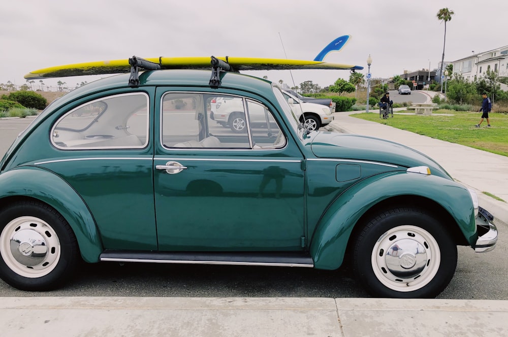 empty green Volkswagen Beetle carrying yellow surfboard on parking lot during daytime