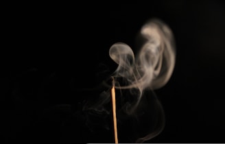 Soft tendrils of colorful incense smoke rising against a deep black background, glowing with hints of warm amber and vibrant violet.