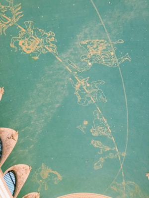 A teal ceiling features golden outlines of constellations and zodiac signs, set against a grid pattern. Architectural arches are visible at the edges with intricate details.