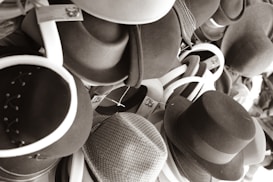A collection of various styles of hats piled together, primarily in shades of gray, black, and white. The hats appear to be made from different materials, including fabric and felt, and some have unique designs or bands.