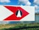 A sign with a large red arrow pointing to the right and a white icon of praying hands in the center is positioned against a backdrop of a grassy area and a body of water. The sky is clear with scattered white clouds.