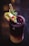 A dark, multicolored beverage in a glass is garnished with lime slices, pomegranate seeds, mint leaves, and served with a straw. The drink features a gradient from deep purple at the top to creamy at the bottom, with a sugared rim.