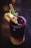 A dark, multicolored beverage in a glass is garnished with lime slices, pomegranate seeds, mint leaves, and served with a straw. The drink features a gradient from deep purple at the top to creamy at the bottom, with a sugared rim.