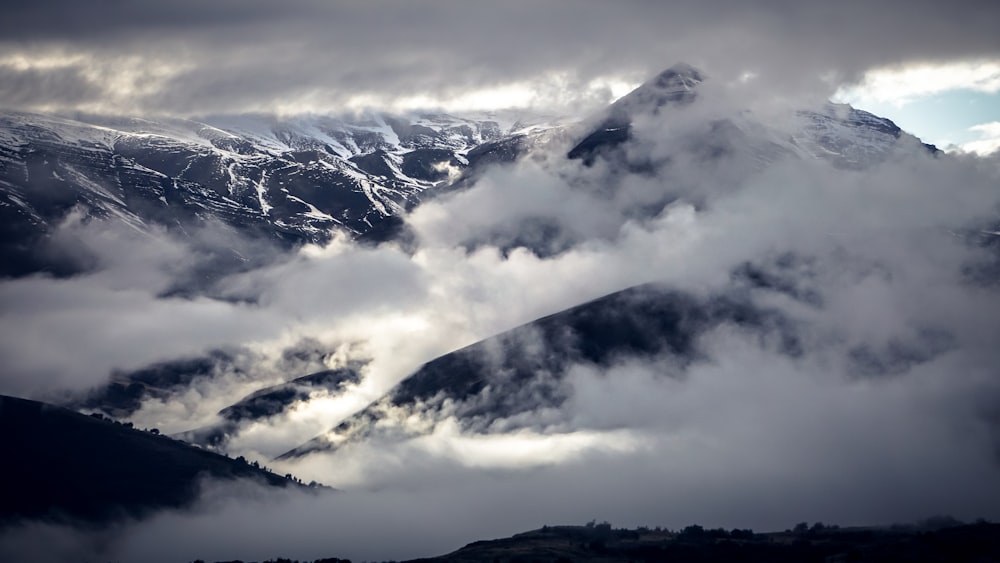 fogs covering rocky mountain under cloudy sky during daytime