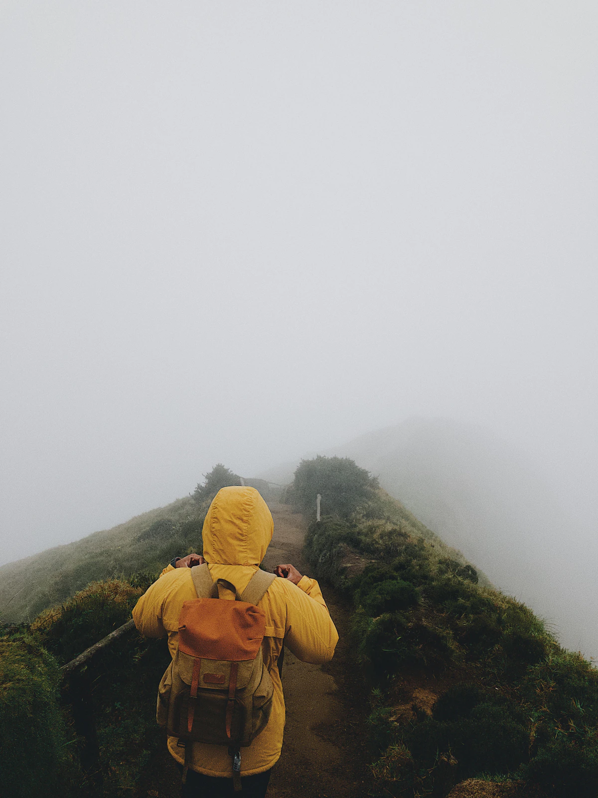 A hiker in a yellow coat stepping into the fog