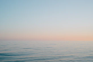 A tranquil ocean horizon at dawn, soft pastel skies meeting calm waters.