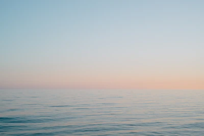 A tranquil ocean horizon at dawn, soft pastel skies meeting calm waters.