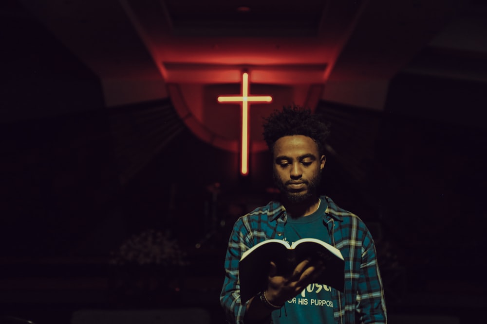 man reading book in front of LED cross