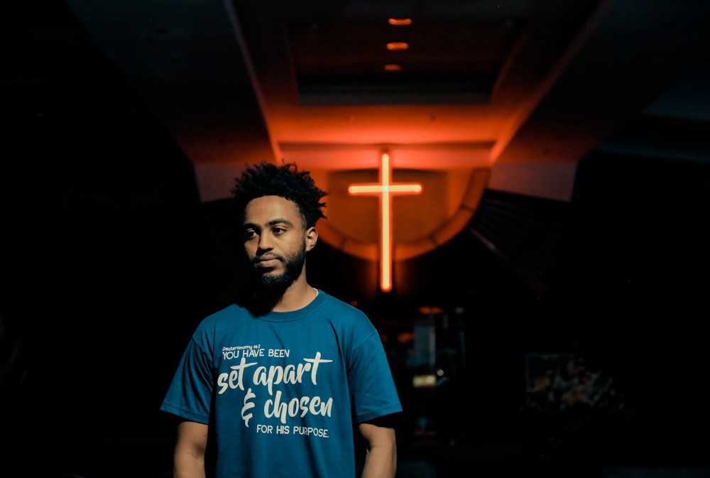 man in blue t-shirt standing beside black wall