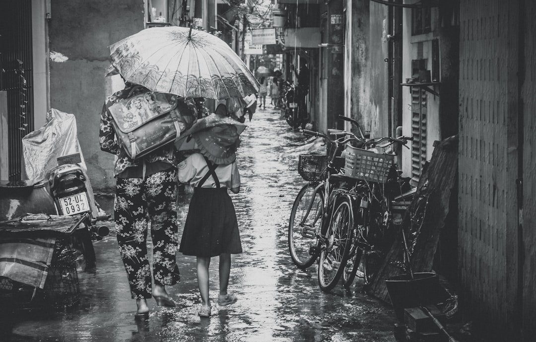 grayscale photography of woman and girl walking while holding umbrella