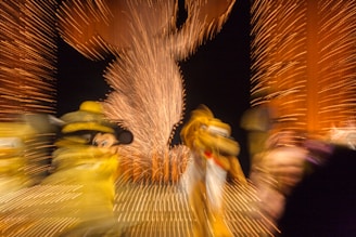 Blurred motion capture of colorful characters amidst a backdrop of vibrant lights, with a central figure outlined by fireworks patterns.