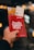 A hand is holding a red Berlin Welcome Card along with some tourist brochures against a blurred background with bright lights. The card features the Berlin skyline in silhouette.