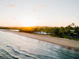 A breathtaking aerial view of a golden sunset over a tropical beach with crystal-clear blue waters.