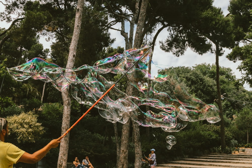 person making large bubbles near trees during daytime