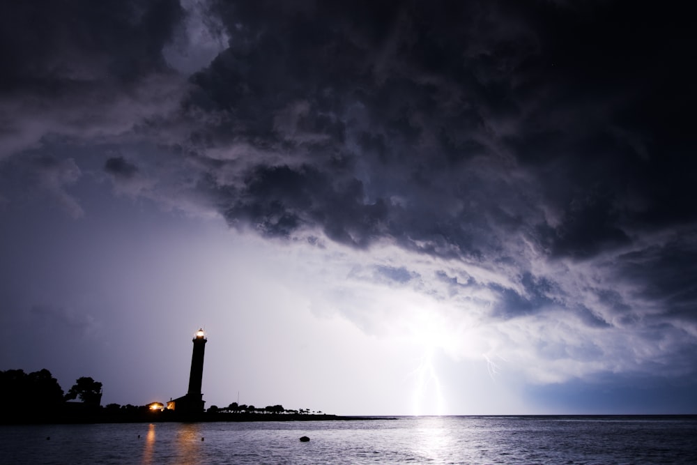 Specchio d'acqua attraverso la silhouette del faro durante la notte