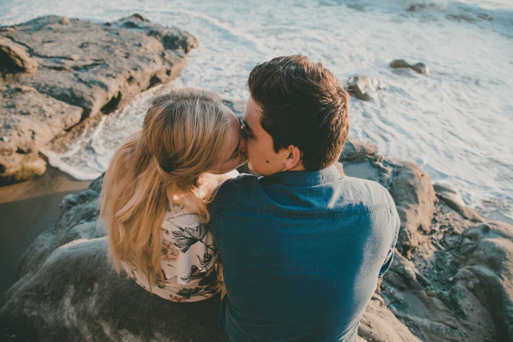 couple kissing white sitting on rock at the beach