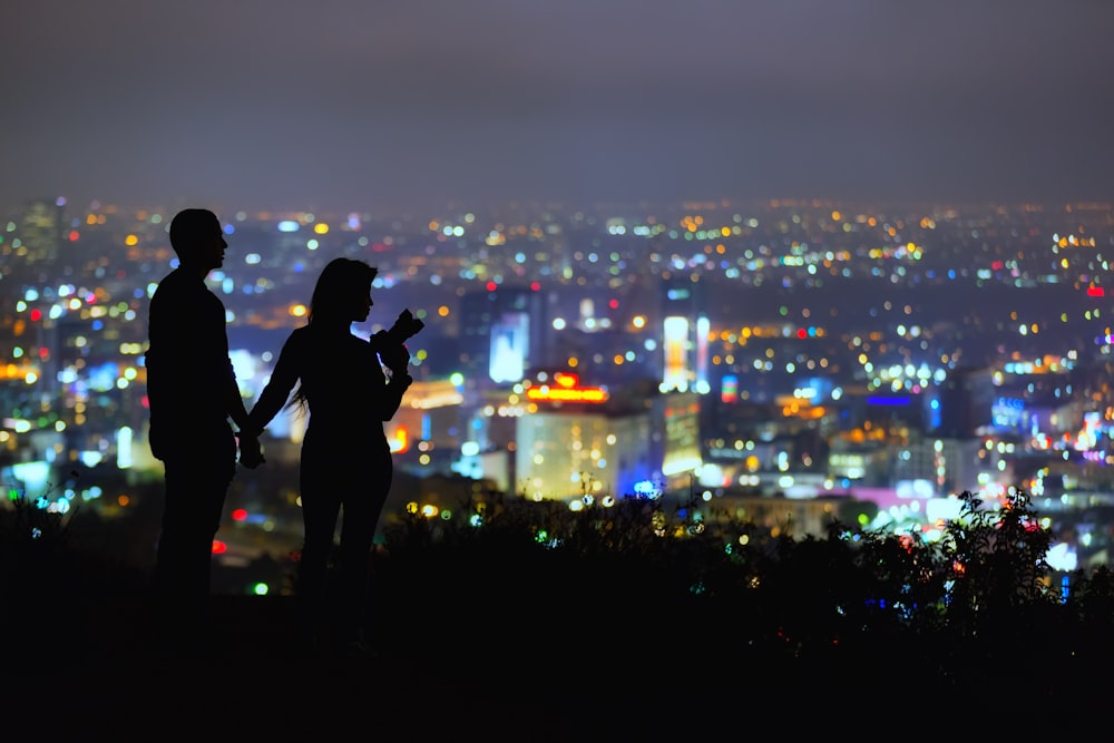 couple standing on hill overlooking city at night