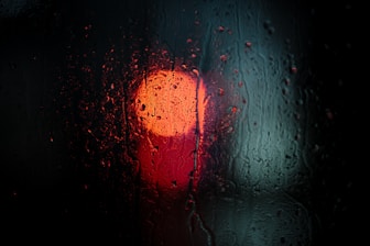 a red traffic light sitting on the side of a rain covered window