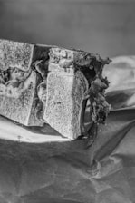 A black-and-white image of a stack of sandwiches with visible fillings on brown paper. The sandwiches appear textured and rugged, with layers of bread and thick fillings.