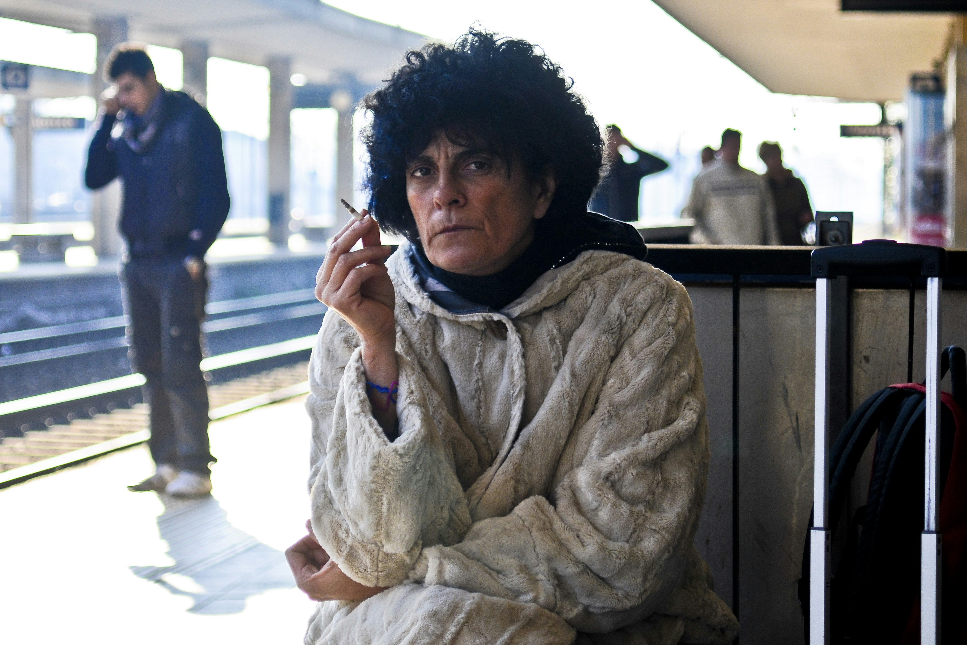 An old, moody lady smoking at a train station.