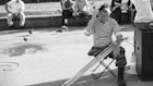 grayscale photo of man sitting on folding stool with crutches in front of people