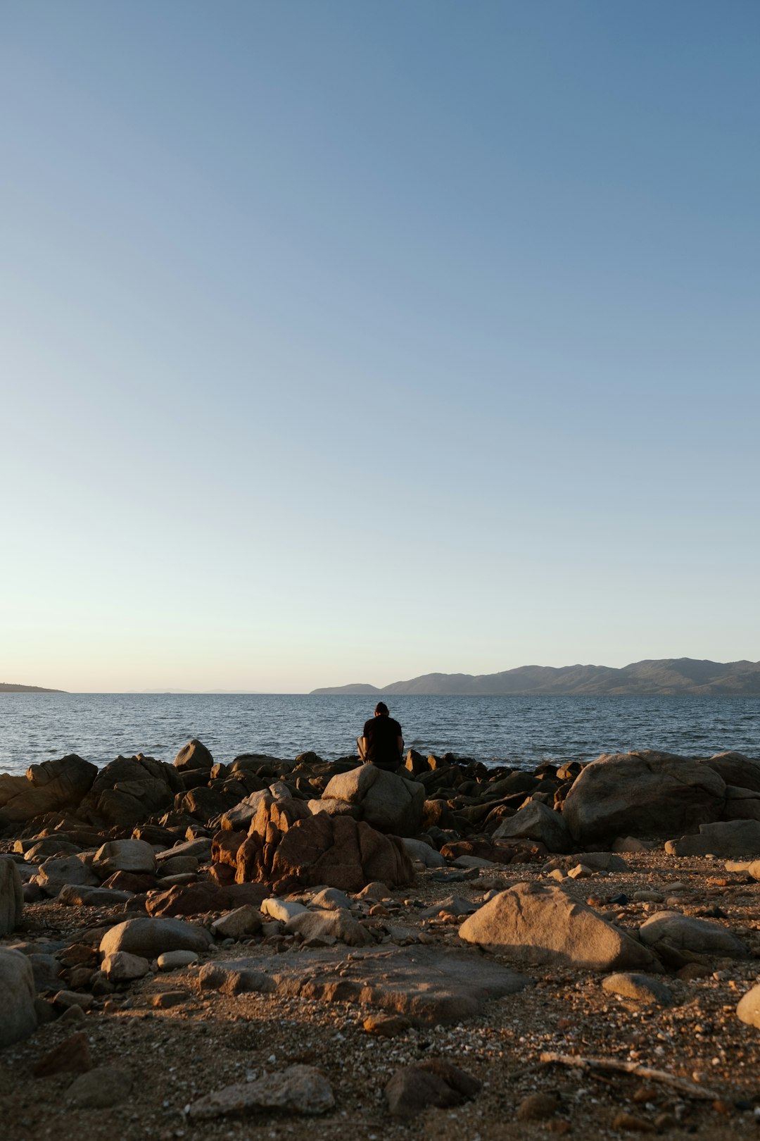 person sitting on rock near seashore during daytime