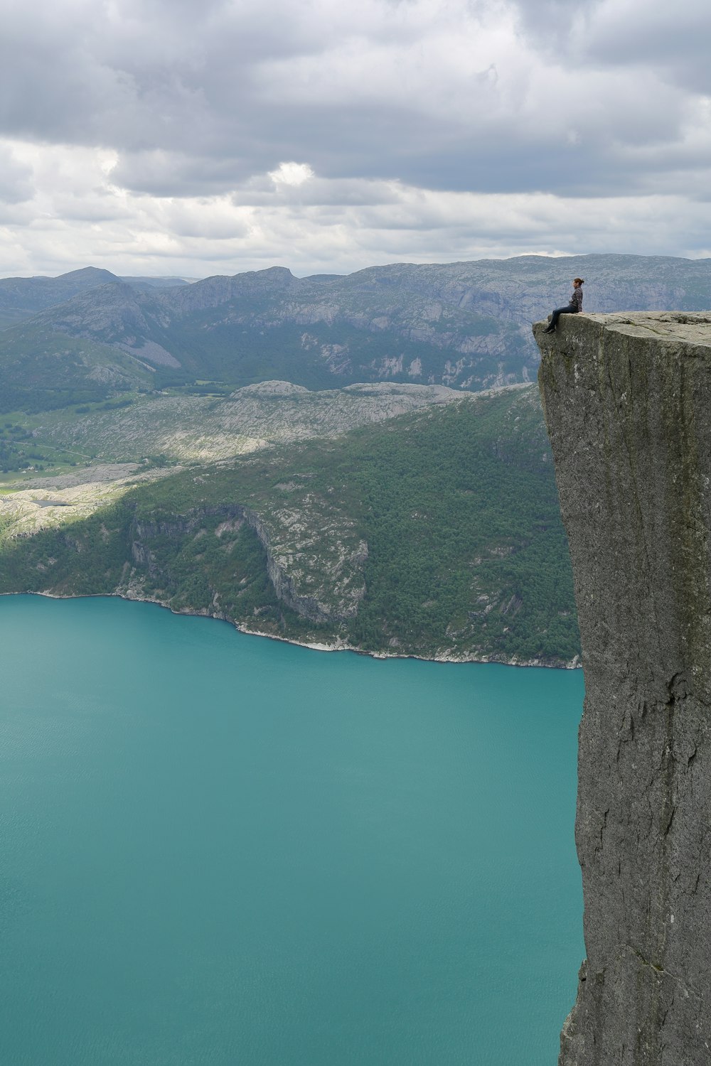 person sits on cliff over the lake