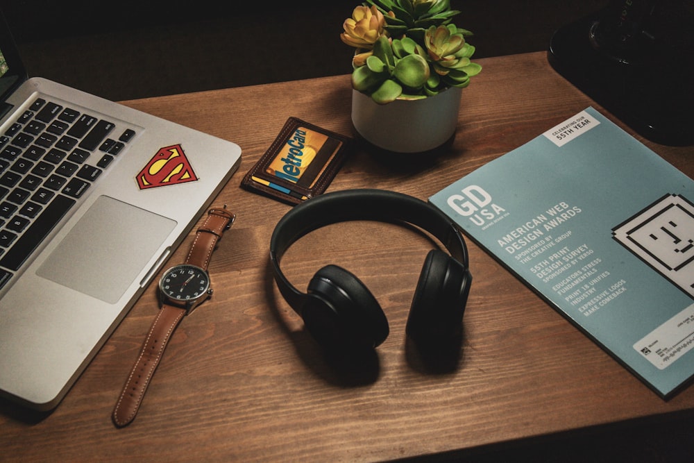 wireless headphones beside magazine, wristwatch, and MacBook Pro