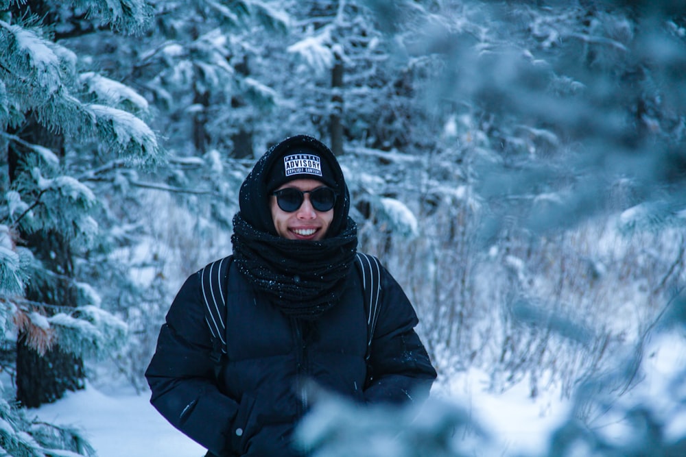 hombre sonriente de pie cerca de los árboles cubiertos de nieve
