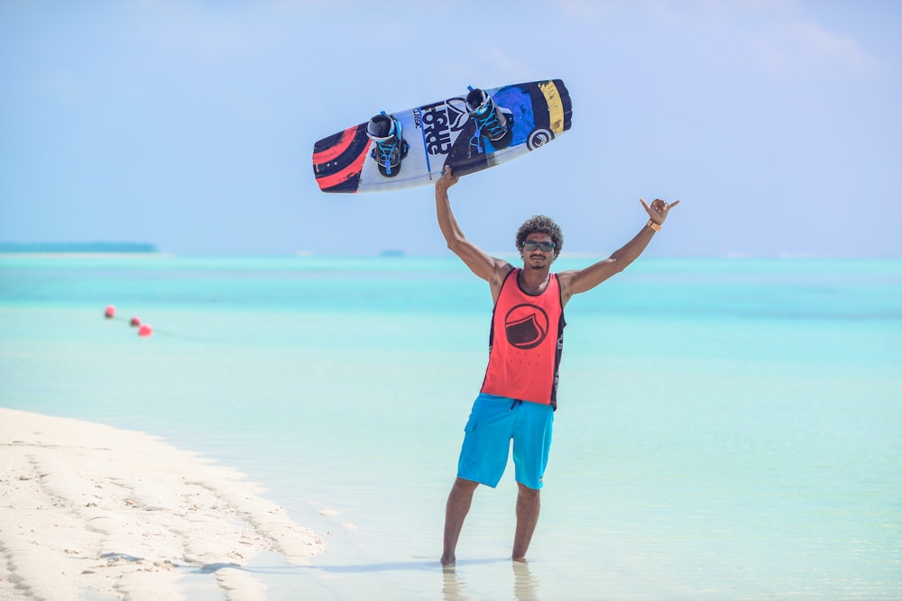 man in red and black tank top standing near seashore holding a board