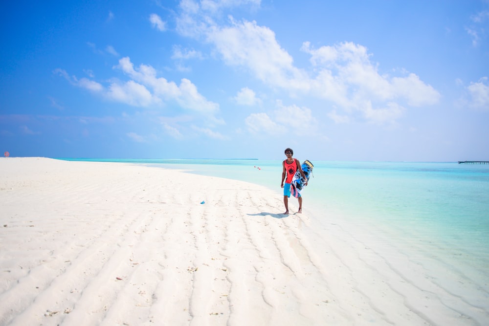 man wearing orange shirt walking on seashore