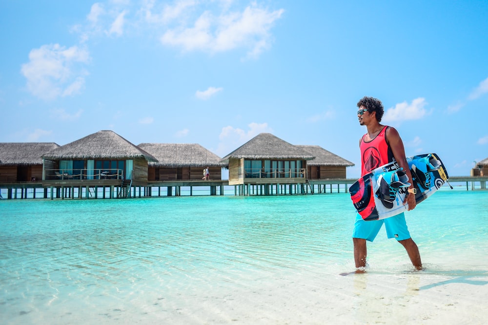 man in red tank top carrying wakeboard during daytime