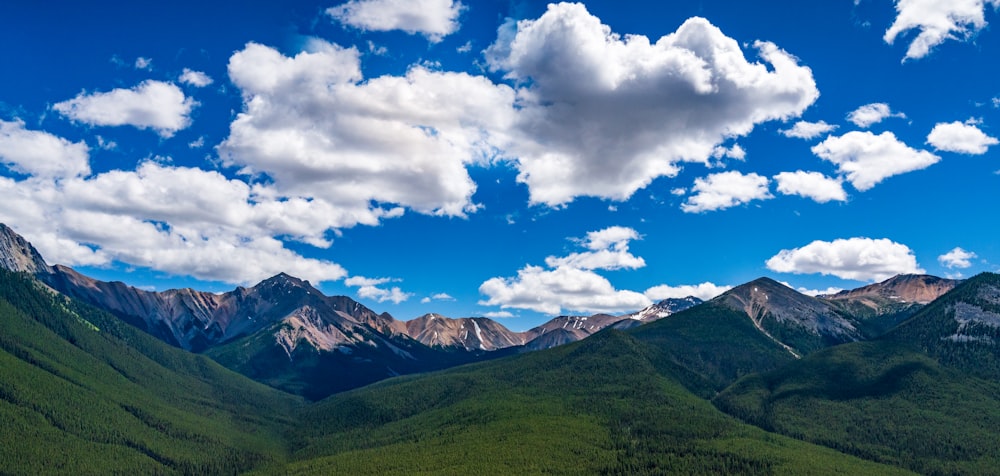 green grass field and mountains under white clouds and blue sky during daytime