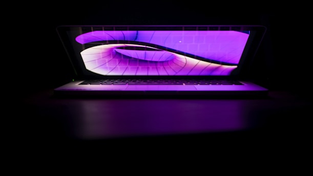 A sleek laptop displaying futuristic tech graphics against a navy blue and dark purple background.