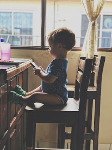 boy holding smartphone while sitting on the chair