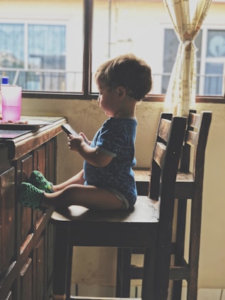 boy holding smartphone while sitting on the chair