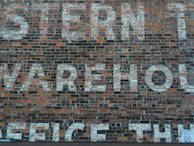 Close-up of aged factory bricks with faded painted signage from the early 1900s.