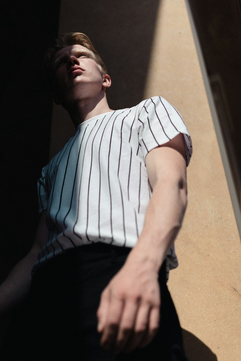 man wearing white striped shirt leaning on wall