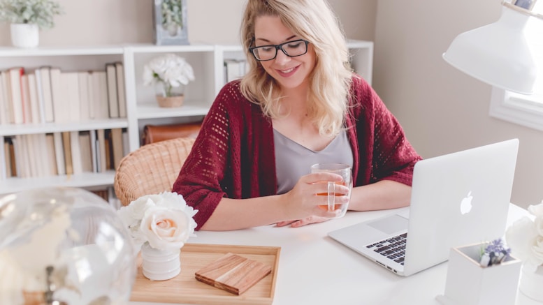 woman smiling holding glass mug sitting beside table with MacBook